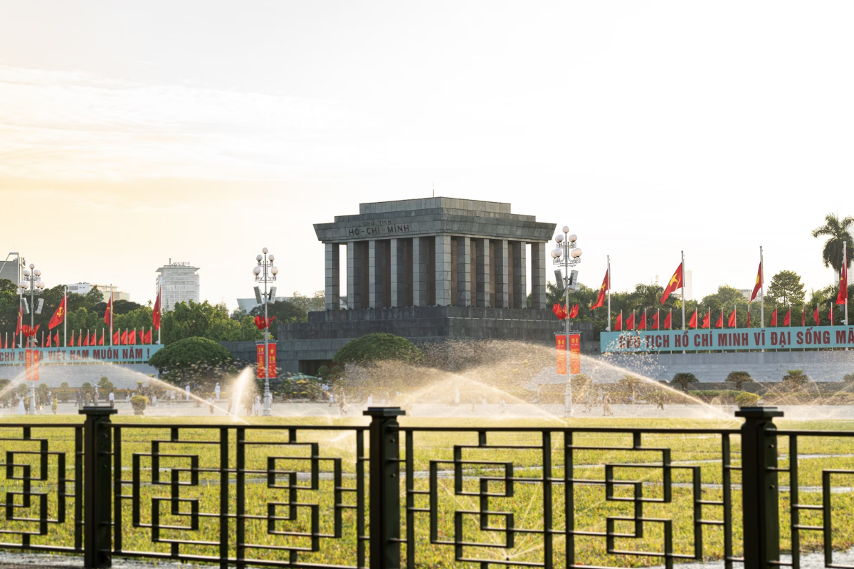Ho Chi Minh Mausoleum in Hanoi with Vietnamese flag and uniformed guards during the day.